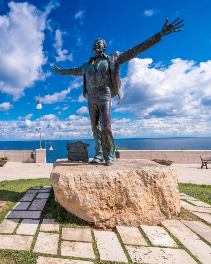 Statua di Domenico Modugno sul lungomare di Polignano a Mare con vista panoramica sul mare