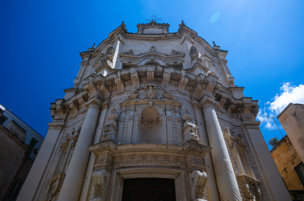 Facciata barocca di una chiesa storica nel centro di Lecce vista dal basso contro il cielo azzurro