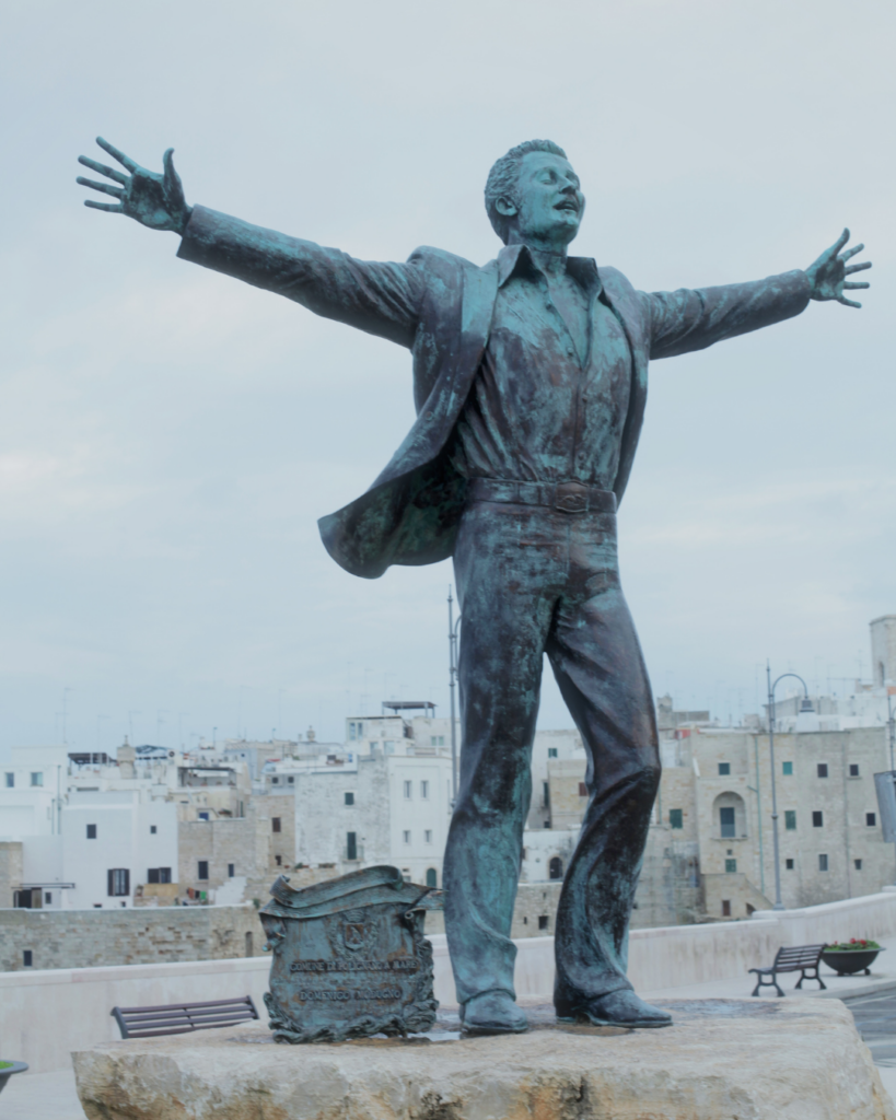 Statua di Domenico Modugno a Polignano a Mare con il borgo sullo sfondo