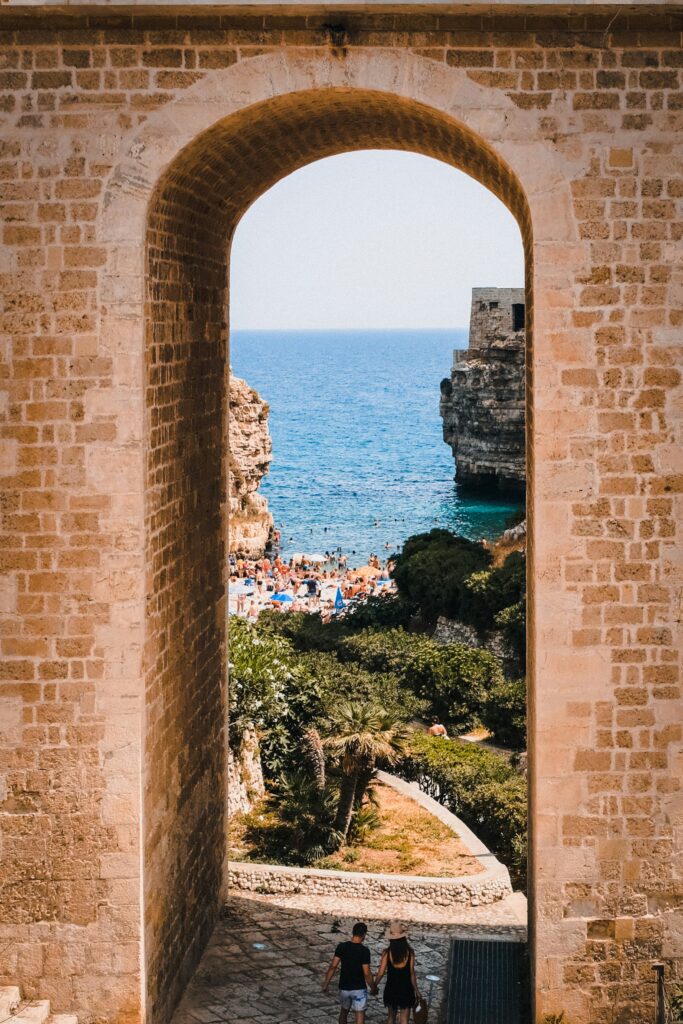 Scorcio di Polignano a Mare attraverso un arco in pietra con vista sulla cala e sul mare